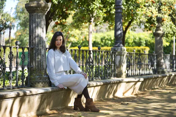 Genç, güzel, siyah saçlı, beyaz elbiseli, rahat ve sakin bir kadın, bir bankta tek başına oturuyor. Güzelliği, modayı, eğilimi, kadınlığı kavra.