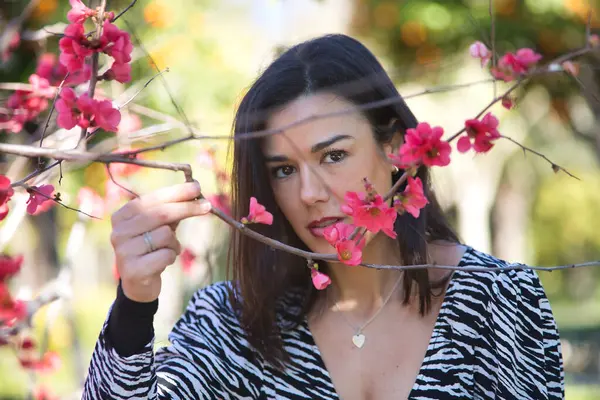 Genç, güzel, siyah saçlı, zebra elbiseli bir kadının portresi, yüzünü dallar ve Japon ayva çiçekleri ile kaplıyor. Güzelliği, modayı, eğilimi, dişiliği, doğayı, ağaçları kavra.