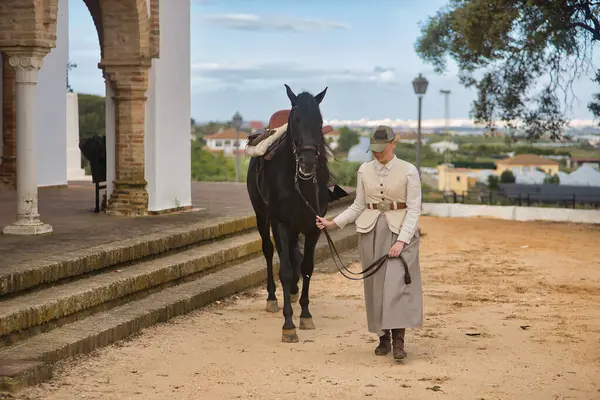 Siyah İspanyol safkan atıyla yürüyen genç bir kadın binici dizginleri elinde tutuyor. Konsept at biniciliği, at biniciliği, binicilik, binicilik.