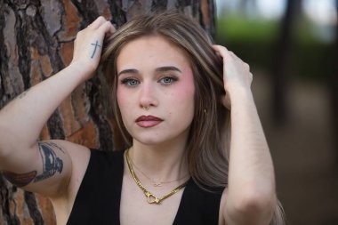 Genç, güzel bir kadının portresi, sarışın, yeşil gözlü, siyah bluzlu, bir ağacın gövdesine yaslanırken kameraya tatlı ve nazikçe bakan. Masumiyet kavramı.