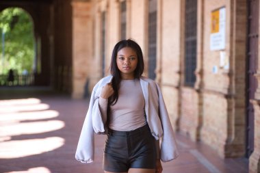 Genç, güzel, Afrikalı bir kadın, ceketli ve deri şortlu, İspanya meydanında poz veriyor ve modellik yapıyor. Moda konsepti, güzellik, moda.