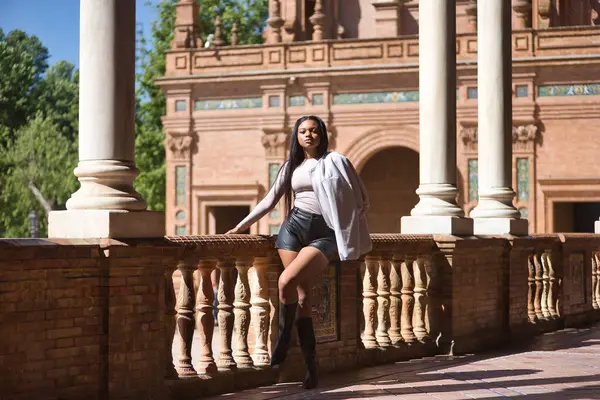 Genç, güzel, Afrikalı bir kadın, ceketi, deri şortu ve botları var, Sevilla 'da İspanya meydanında model olarak poz veriyor. Moda konsepti, güzellik, moda.