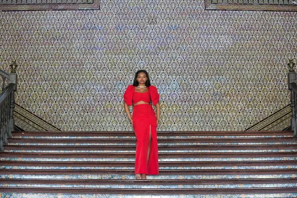 Genç, güzel, Afrikalı bir kadın, kırmızı bir elbise giyiyor, Sevilla 'daki İspanyol meydanının merdivenlerinde mankenlik yapıyor. Moda konsepti, güzellik, moda.