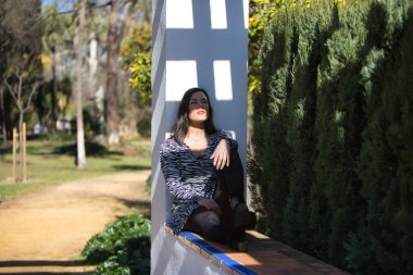 Genç, güzel, siyah saçlı bir kadın, zebra elbisesi içinde, gözleri kapalı, oturuyor ve sırtı bir sütunun üzerinde dinleniyor, güneş ışınlarını yüzüne alıyor. Kavramsal ışıklar, gölgeler.