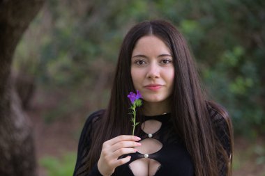 Soluk tenli, esmer bir kadının portresi, siyah bir elbise giyiyor, elinde tuttuğu menekşe çiçekle yüzünü okşuyor, baharın gelişini kutluyor..