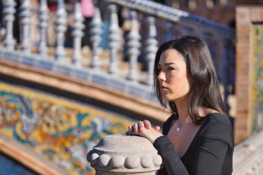 Siyah uzun kollu tişörtlü, genç, güzel, koyu renk saçlı bir kadının portresi. Dalgın ve konsantre. Elleri bir balkonun üzerinde dinleniyor. Düşleri, düşünceleri, konsantrasyonu kavra.