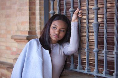 Genç, güzel, Afrikalı bir kadının portresi, ceketli, Sevilla 'da İspanya meydanındaki bir pencerenin ızgarasına yapışan rüya gibi bakışlı. Moda konsepti, güzellik, moda.