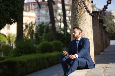 Genç, esmer, İspanyol, modern yönetici, takım elbiseli ve kravatlı, ciddi, ekonomik krizden endişeli ve sıkıntılı, bir şehir caddesinde bazı basamaklarda oturuyor. İş konsepti, şirket, lider.