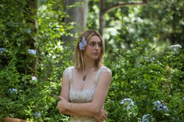 Genç, güzel, sarışın bir kadının portresi, çiçekli bir elbise giyiyor, uzaktan bakıyor, saçında bir buket menekşe ile, açık hava parkında. Güzellik kavramı, gençlik, milenyum.