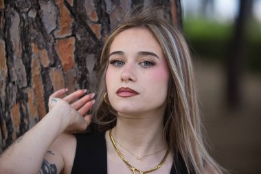 Genç, güzel bir kadının portresi, sarışın, yeşil gözlü, siyah bluzlu, bir ağacın gövdesine yaslanırken kameraya tatlı ve nazikçe bakan. Masumiyet kavramı.