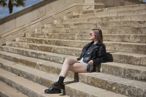 Genç, güzel, sarışın, deri ceketli, yılan desenli mini etekli, çizmeli ve güneş gözlüklü, rahat ve sakin güneşlenen, merdivenlerde oturan. İsyankar, boyun eğmez, isyancı konsept.