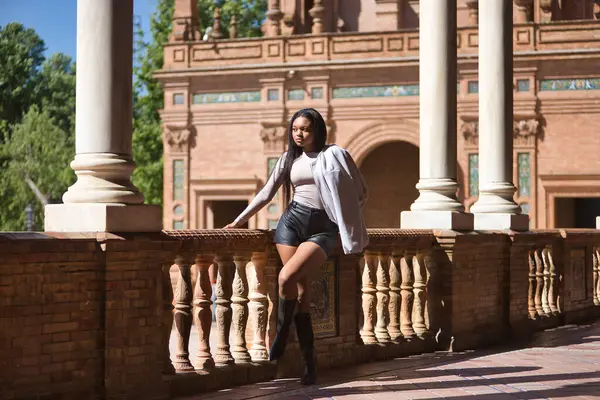 Genç, güzel, ceketli, deri şortlu, botlu, İspanya meydanındaki korkuluklara yaslanmış genç, Afrikalı bir kadın. Moda konsepti, güzellik, moda.