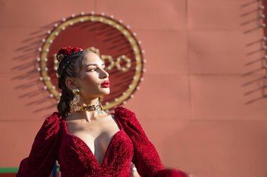 Genç, sarışın bir kadın, kırmızı flamenko elbisesi, saçında çiçekler ve altın mücevherlerle Sevilla 'daki fuarın kapağında flamenko pozları veriyor. HAYIR ve DO, Kral Alfonso X 'in sembolüdür..