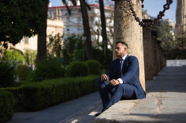 Genç, esmer, İspanyol, modern yönetici, takım elbiseli ve kravatlı, ciddi, ekonomik krizden endişeli ve sıkıntılı, bir şehir caddesinde bazı basamaklarda oturuyor. İş konsepti, şirket, lider.