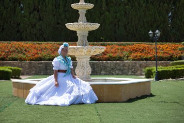 Genç, güzel, sarışın bir kadın tipik Endülüs flamenko kostümlü açık hava parkındaki güzel bir çeşmede açık mavi şallı ve çiçekli bir hac yolculuğu için bekliyor..