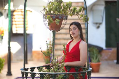 Kırmızı parti elbisesi içinde genç, güzel, esmer bir kadın, rahat poz veriyor ve sakince eski bir su kuyusuna yaslanıyor. Güzellik, moda, moda, gençlik kavramı.