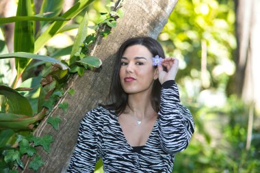 Genç, güzel, siyah saçlı, zebra elbiseli, mutlu ve gülümseyen, kulağına menekşe takan bir kadının portresi. Güzellik, moda, eğilim, kadınlık, doğa, bitkiler, çiçekler.