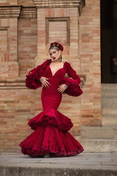 Genç, güzel, sarışın, kırmızı flamenko elbiseli, saçında çiçekler ve altın mücevherlerle İspanya meydanında flamenko dansı yapan bir kadın. Dans konsepti, sanat. Dikey konum.