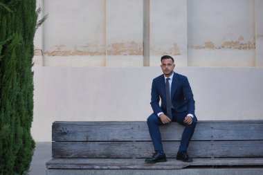 Genç, esmer, İspanyol, modern yönetici, takım elbiseli ve kravatlı, ekonomik kriz konusunda ciddi ve endişeli, mola alıyor, kentteki ahşap bir bankta oturuyor. Konsept iş, şirket, lider.