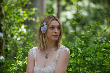 Genç, güzel, sarışın bir kadının portresi, çiçekli bir elbise giyiyor, uzaktan bakıyor, saçında bir buket menekşe ile, açık hava parkında. Güzellik kavramı, gençlik, milenyum.