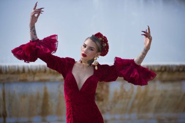 Genç, güzel, sarışın, kırmızı flamenko elbiseli, saçında çiçekler, altın mücevherler, Seville 'de İspanya meydanında fıskiyeli fıskiyelerle flamenko pozları veriyor..