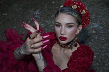 Genç, güzel, sarışın bir kadının portresi, kırmızı flamenko elbisesi, saçında çiçekler ve altın takılar, yukarıdan yakından flamenko pozları veriyor. Konsept dansı, sanat, tipik İspanyol..