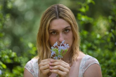 Genç, güzel, sarışın bir kadının portresi, çiçekli bir elbise giyiyor, tatlı ve narin bir bakışla, açık hava parkında bir buket menekşe kokluyor. Güzellik kavramı, gençlik, milenyum.