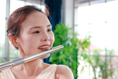 Krem rengi elbise giyen Asyalı kadın uluslararası bir rüzgar enstrümanı olan flüt çalıyor. Klasik şarkılar çal. Bir grupta klasik müzik çalan konserler. müzik öğrenme