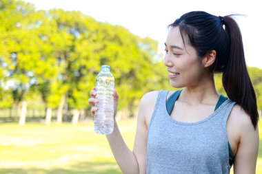 Güzel Asyalı kadınlar sağlığa bayılır. Sabah parkta egzersiz yapıyor idmandan sonra vücudunu tazelemek için bir şişe su tutuyor. sağlık hizmeti kavramı