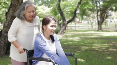 Yaşlı bir anne engelli kızı için tekerlekli sandalye itiyor, yürüyemiyor. Parktaki temiz havayı içine çek. Aile kavramları, sağlık hizmetleri.
