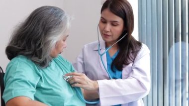 Asyalı kadın doktor, depresyon geçiren yaşlı hastaları muayene etmek için steteskop kullanıyor. Tekerlekli sandalyede oturuyormuş. Kıdemli hastalar kavramı. Yaşlılar Sağlık Merkezi