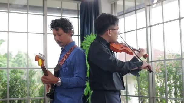 2人のアジアの音楽家が練習室でクラシック楽器のバイオリンとエレキギターを演奏する ライブ音楽とバンドの演奏の概念 音楽はレコーディングスタジオで演奏されています — ストック動画