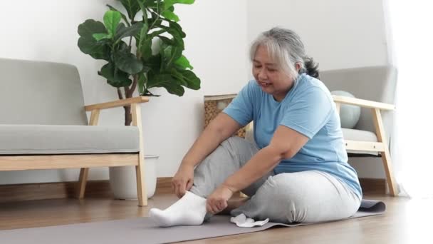 自宅で運動するアジア系のお年寄り足の怪我を防ぐために靴下を履いて座っていました 退職後の医療の概念は — ストック動画