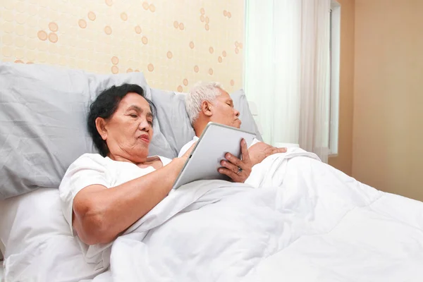 Asian elderly couple lying in bed in the bedroom elderly woman insomnia Look at social media online. family concept health care, health insurance for seniors