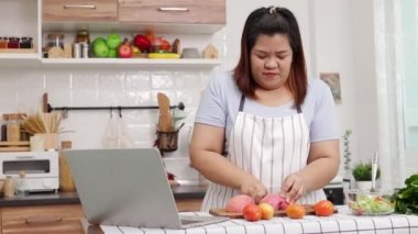 Fat Asian woman cooking in the kitchen Learn to make salads and healthy food from social media. health care concept Eat healthy food to lose weight.