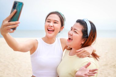 İki şişman ve zayıf Asyalı kız ellerinde akıllı telefonlarla selfie çekerek deniz yolculuğunun tadını çıkarıyorlar. Seyahat eden kadın. Seyahat ve yaşam tarzı kavramı