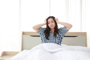 Güzel Asyalı kadın yatakta yatıyor, elleriyle başını tutuyor, stres altında, uykusuzluk çekiyor. sağlık hizmeti kavramı