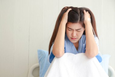 Stresli Asyalı kadın hasta hastane yatağında başını tutuyor. Sağlık sigortası yaptırıyorum. kadın sağlığı sorunları
