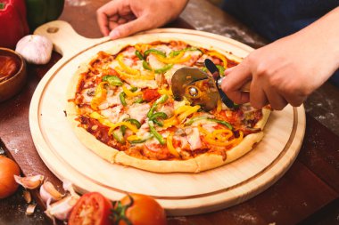 Şef, yuvarlak ahşap tepsiye yerleştirilmiş ev yapımı İtalyan pizzalarını kesmek için paslanmaz çelik bıçaklar kullanır. Fast food konsepti. Üst görünüm.