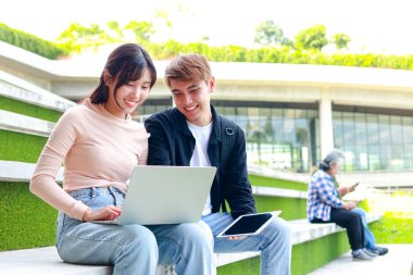 Asyalı üniversite öğrencileri çalışmak ve sınavlara hazırlanmak için dizüstü bilgisayar kullanırlar. Ya da bir grup projesinde çalışırken. Kampüsteki beton zeminde otururken. Eğitim konsepti. Boşluğu kopyala