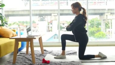 Güzel Asyalı kadın egzersizini apartman dairesinde yaptı. Antrenörü takip eden egzersizleri dizüstü bilgisayarındaki çevrimiçi videolar vasıtasıyla yaptı. Sağlık hizmeti kavramı, yeni normal