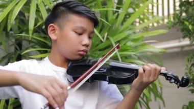 Asyalı çocuk evdeki bahçede klasik bir enstrüman olan keman çalar. Klasik müzik eğitimi konsepti. Müzikal becerileri geliştiriyorum. canlı performans