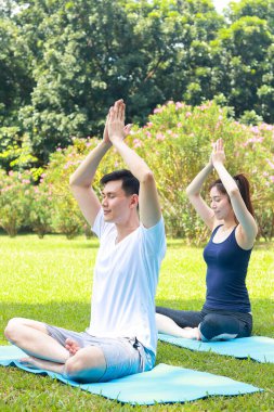 Asyalı çift parktaki çimlerin üzerinde yoga yapıyor ve birlikte egzersiz yapıyor. Spor konsepti. Sağlıklı bir vücudu korumak.