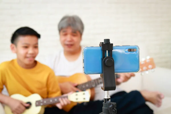亚洲父亲和儿子一起在社交媒体上通过智能手机摄像头现场直播音乐 音乐概念 现代家庭活动 — 图库照片