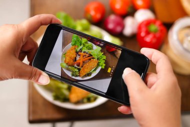 Bir adam masaya yerleştirilen yemeğin fotoğrafını çekmek için siyah bir akıllı telefon kullanıyor. Yiyecek konsepti.