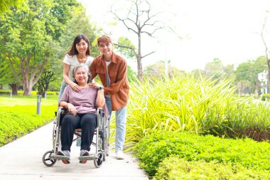 Aile kavramı. Kız ve oğlu, yaşlı anneyi tekerlekli sandalyeye oturtup açık hava parkında temiz hava aldırıyor. Yaşlı sağlık hizmetleri. Boşluğu kopyala