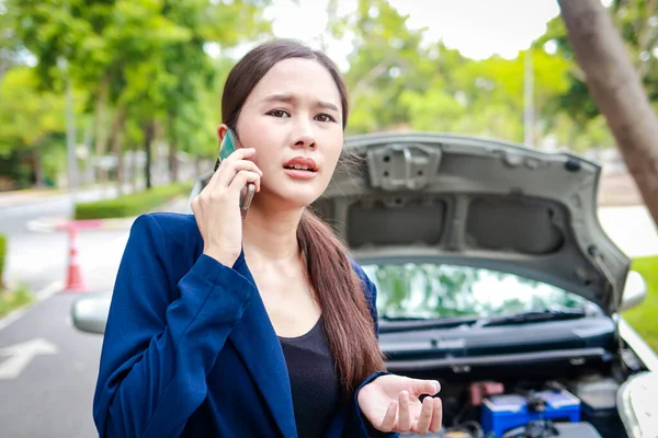 Beautiful Asian woman, broken car on the road Hold a smartphone to inform the insurance company to call for emergency assistance. Concept of car insurance. car service. transportation