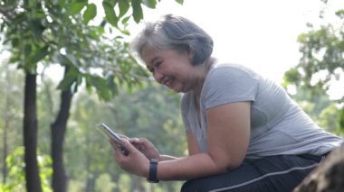 Yaşlı kadın mutlu Asyalı sabah bahçemde akıllı telefonumun başında oturuyor. Egzersiz konsepti. Mutlu olmak için emeklilikte yaşamak. İletişim teknolojisi. Sosyal ağ.