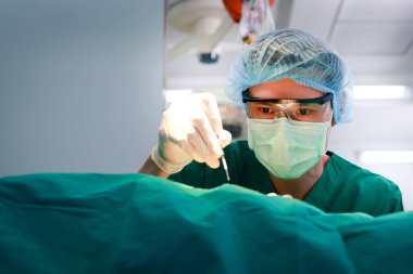 Elinde neşter tutan yeşil üniformalı bir cerrah ya da doktor hastanede ameliyat yapar. Acil ameliyat. karın ameliyatı