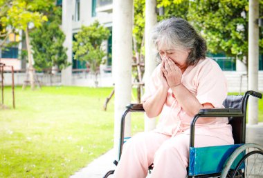 Yaşlı bir Asyalı kadın hasta, hastanede tekerlekli sandalyede oturuyor ve hastalığından pişmanlık duyuyor. Yaşlı hastalık konsepti, sağlık sigortası